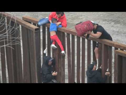 Families with young children attempt to climb Mexico-US border fence